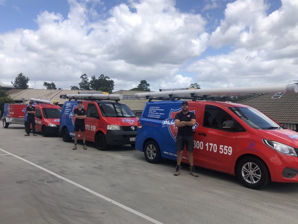 Three plumbers stood in line next to their The Plumbing Gang branded vehicles