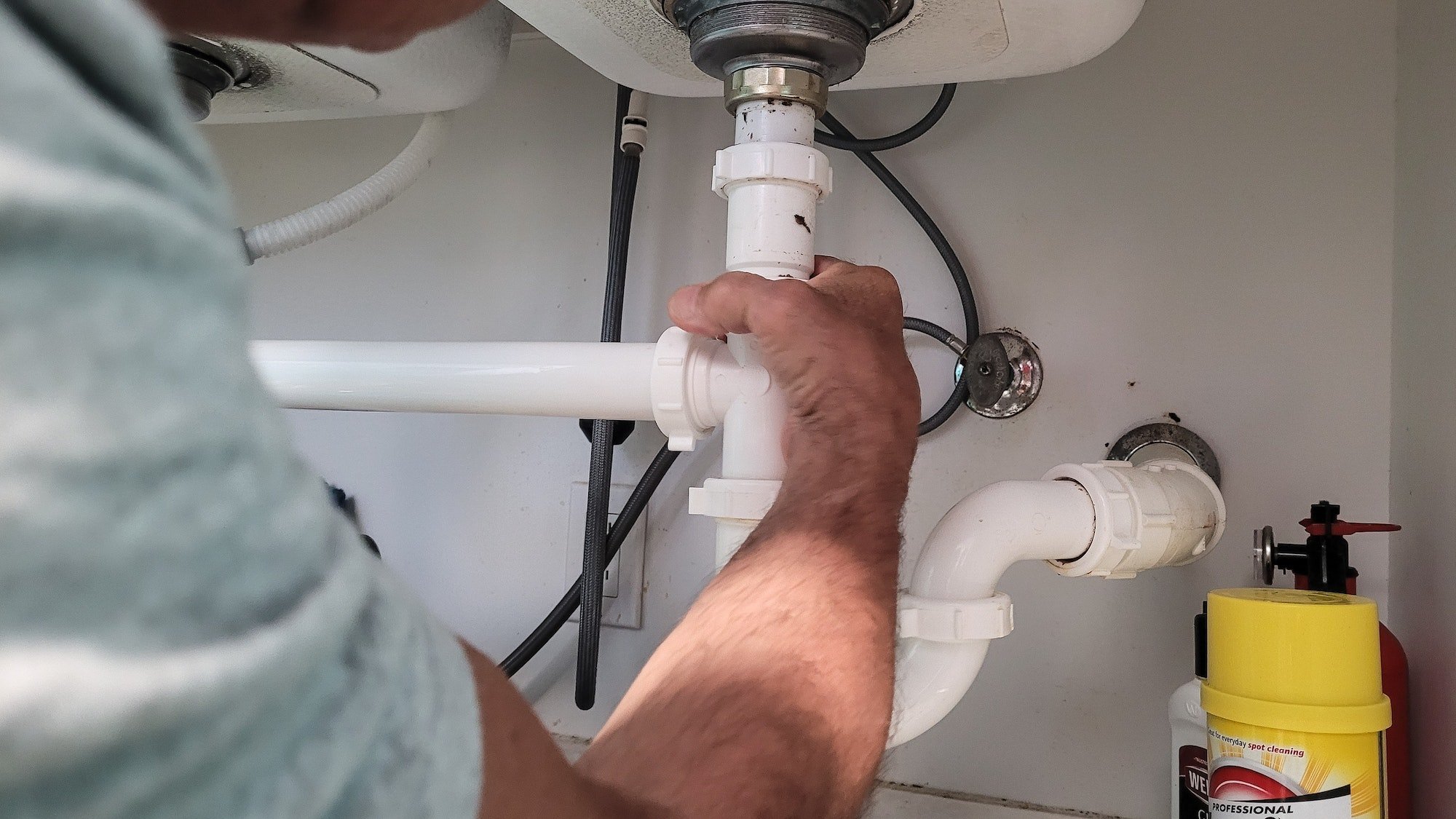 Handyman at home tightening seals on plumbing pipes to stop a leak at kitchen sink.