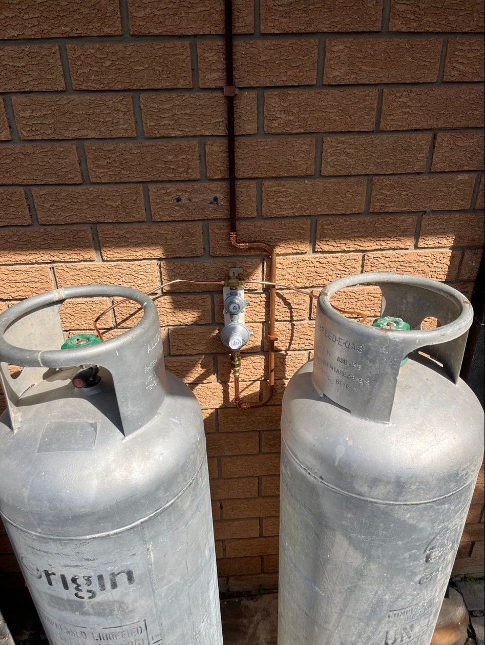 Two gas tanks properly installed on the side of brick house.