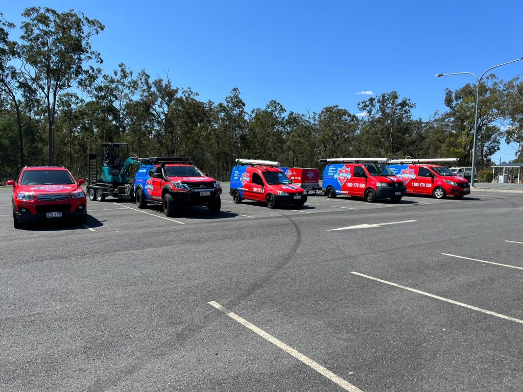 Fleet of The Plumbing Gang branded vehicles parked in a row in a parking lot.